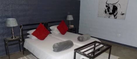 A bedroom with a bed, two nightstands, a lamp, a red pillow, a grey pillow, a wall art of a bull, and a wooden bench.