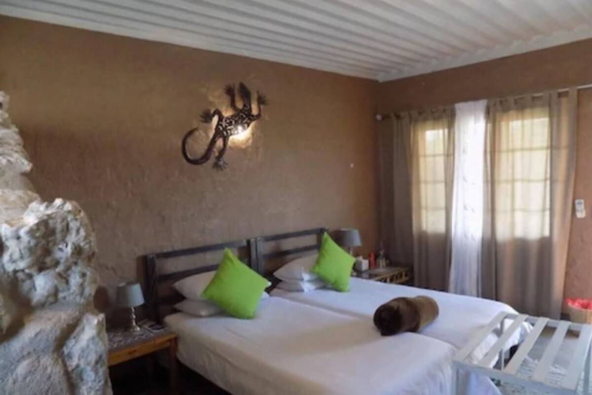 A bedroom with two beds, a stone wall, a wall-mounted light fixture, and a window with curtains.