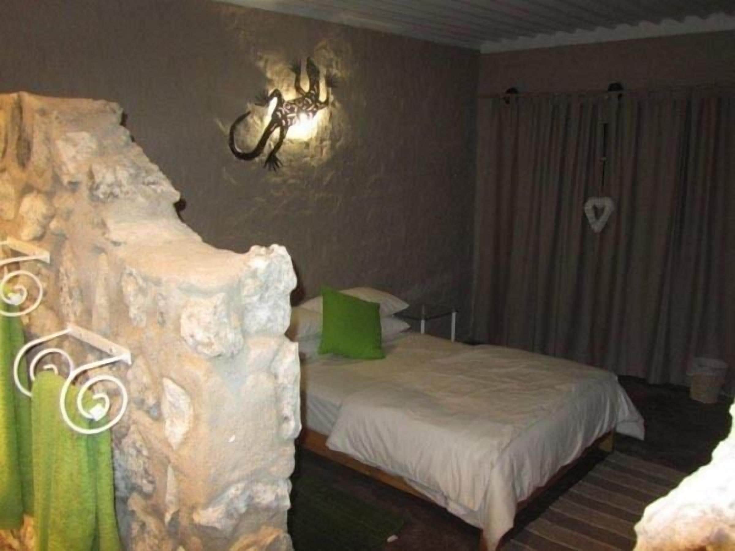 Un dormitorio con pared de piedra, una cama con ropa de cama blanca, un cojín verde y una lámpara de pared.