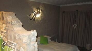 Un dormitorio con pared de piedra, una cama con ropa de cama blanca, un cojín verde y una lámpara de pared.