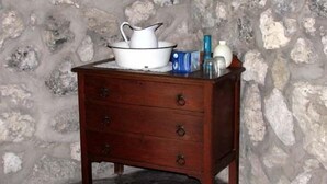 Una mesita de noche de madera con tres cajones frente a una pared de piedra.