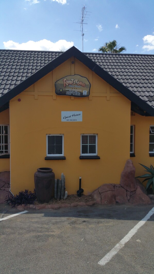 Um edifício amarelo com uma placa indicando "Guest House" e uma placa menor acima com a inscrição "Fintstones Central Reservation".