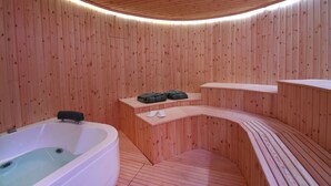 A wooden spa room with a hot tub, benches, and a shelf with towels. - Coconut Villa (Alimos)