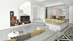 A modern living room with a flat-screen TV, a sofa set, a dining area with a table and chairs, and a staircase leading to an upper level. - Coconut Villa (Alimos)