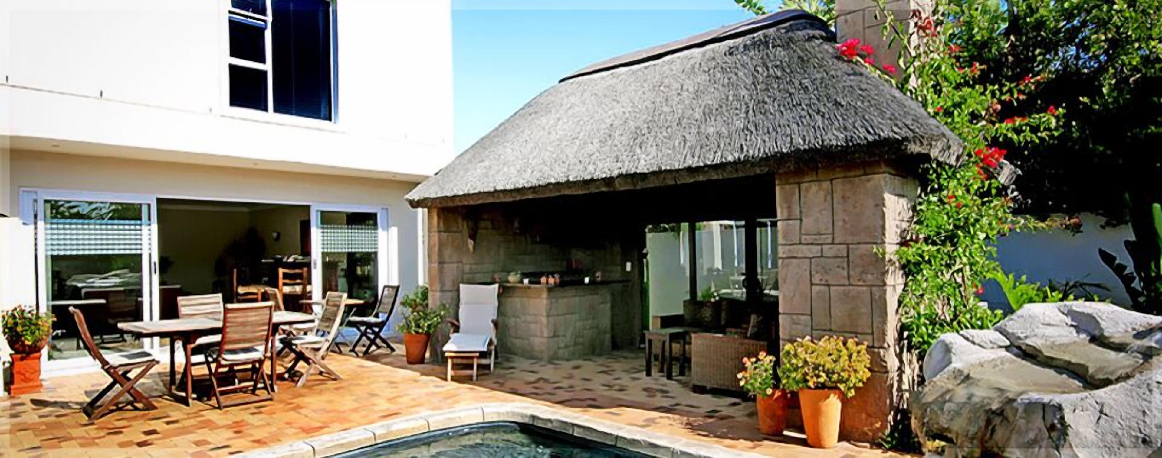 A poolside area with a thatched-roof structure, outdoor seating, and potted plants.