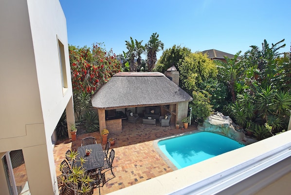 A backyard with a swimming pool, patio furniture, and a thatched-roof outdoor seating area.