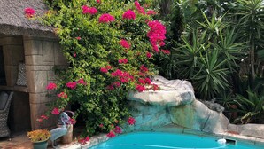 A swimming pool with a stone edge, surrounded by lush greenery and pink flowers. - Atlantic Breeze (Cape Town)