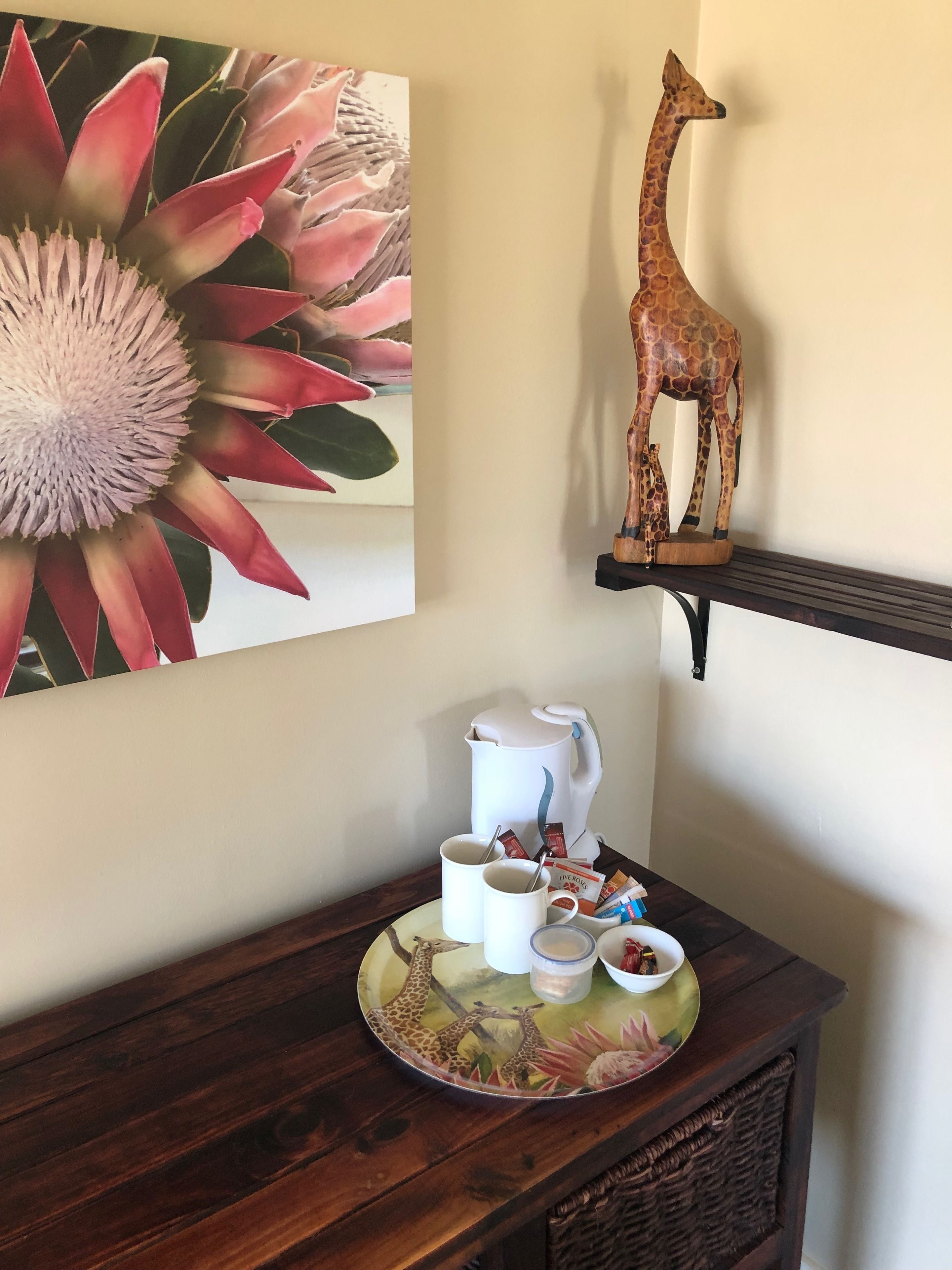 Un tavolo di legno con un vassoio che contiene una caffettiera, tazze e una ciotola di snack. Sul muro è appesa una decorazione a forma di giraffa.