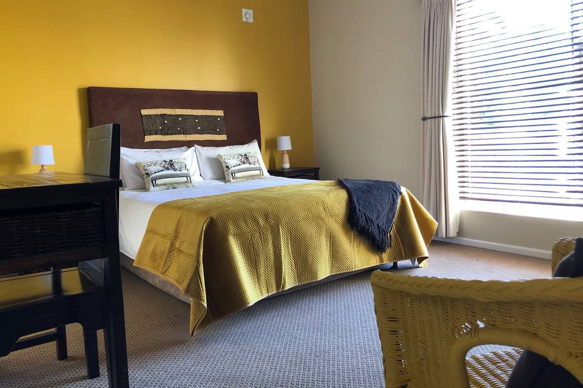 A hotel room with a bed, a desk, a chair, and a window with blinds.