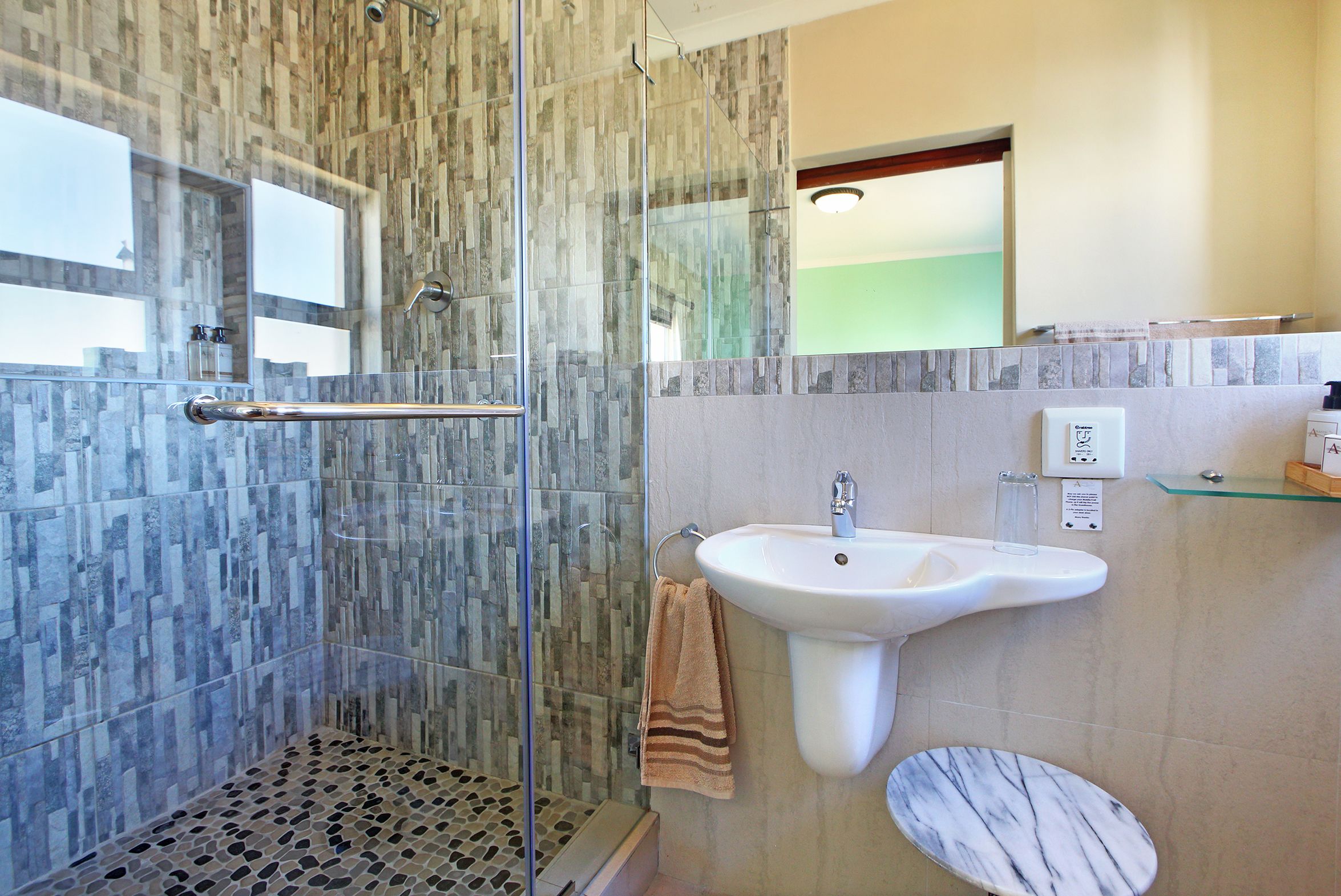 A bathroom with a glass-enclosed shower, a marble sink, and a toilet.