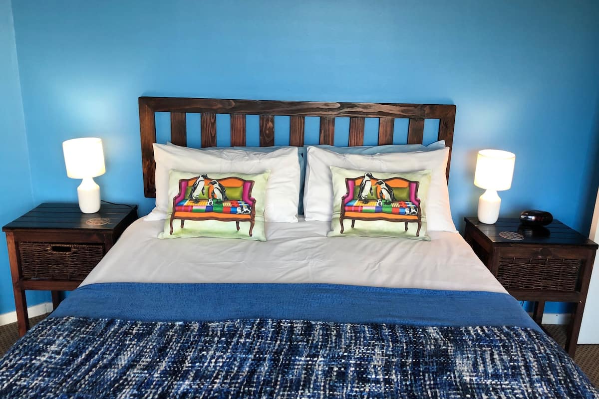 A bed with a blue and white striped blanket, two pillows with penguin illustrations, and wooden headboards against a blue wall.