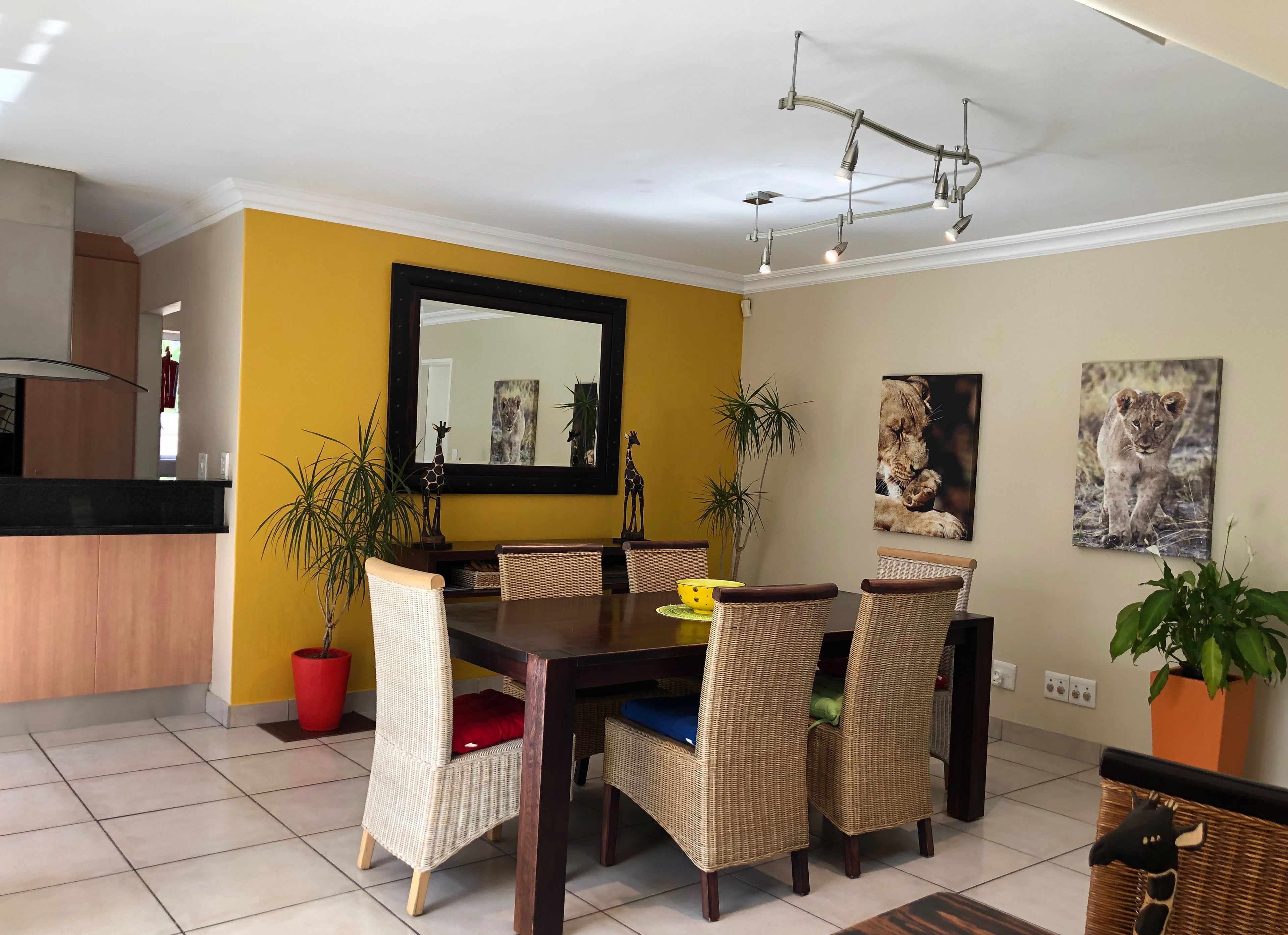A dining area with a dark wooden table, wicker chairs, and a yellow wall.