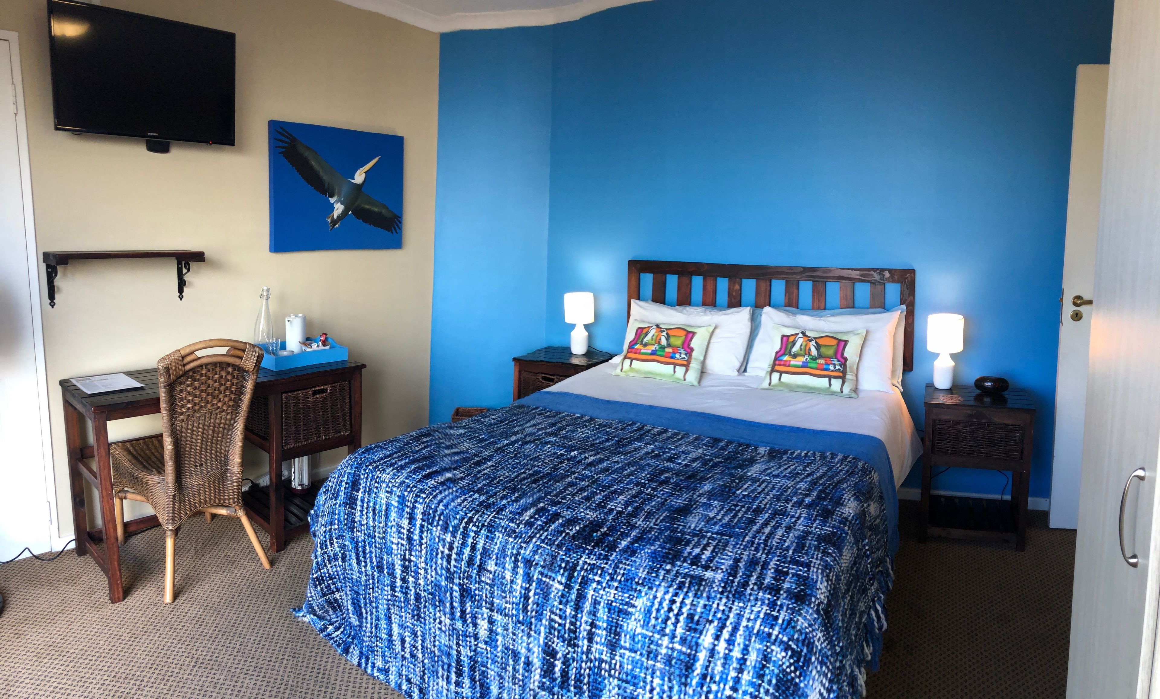 A hotel room with a large bed, a desk, a chair, a television, and a painting of a bird on the wall.