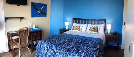 A hotel room with a large bed, a desk, a chair, a television, and a painting of a bird on the wall.