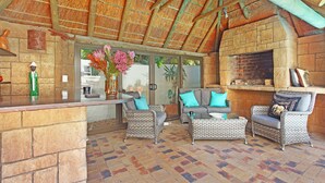 An outdoor patio with wicker furniture, a stone fireplace, and a thatched roof. - Atlantic Breeze (Cape Town)
