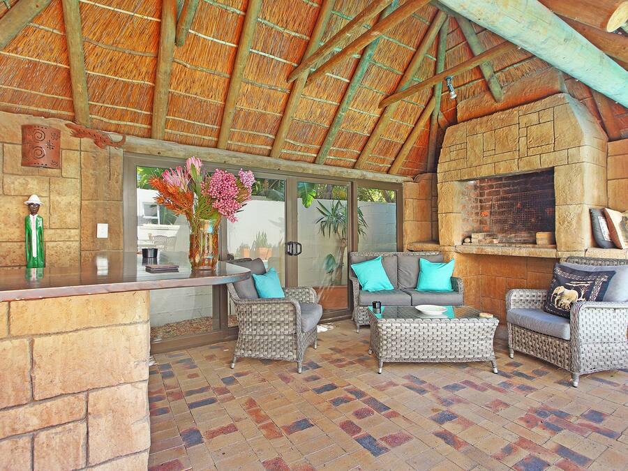 An outdoor patio with wicker furniture, a stone fireplace, and a thatched roof.