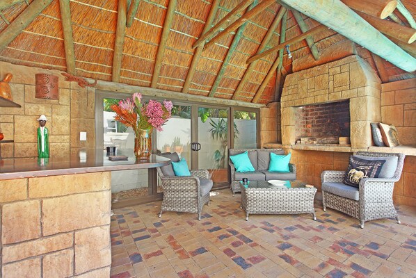 An outdoor patio with wicker furniture, a stone fireplace, and a thatched roof.