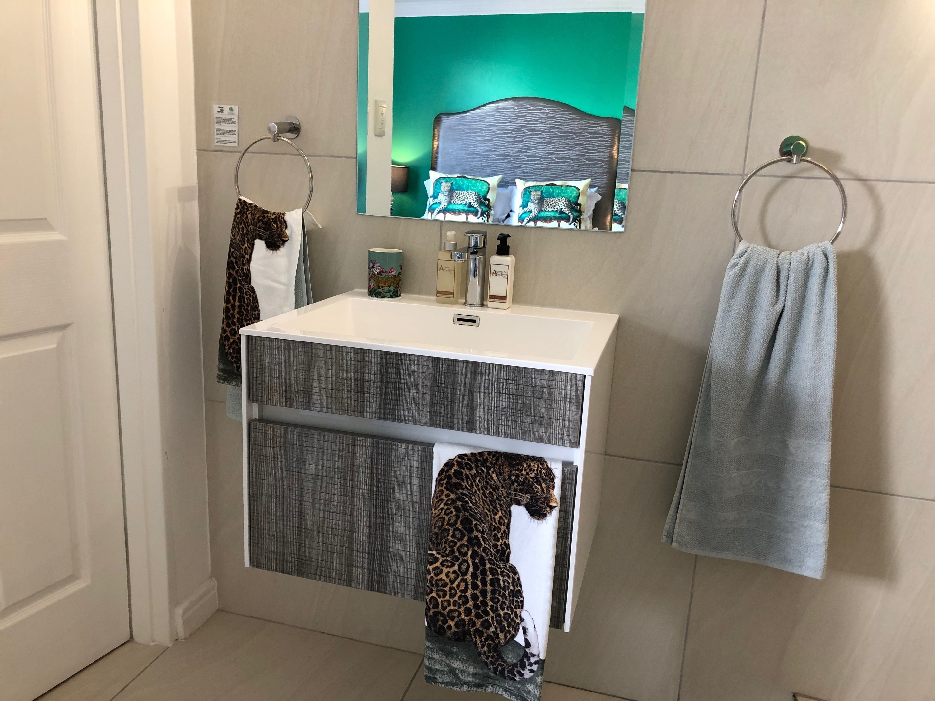 A bathroom with a white sink, a mirror, and two leopard-print towels hanging on towel rings.