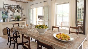 A rustic dining area with a wooden table, chairs, and a bowl of fruit.
