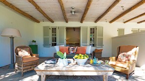 A cozy outdoor seating area with wicker furniture, a table with a bowl of fruit, and a lamp.