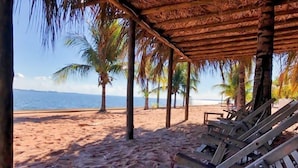 A beach with wooden lounge chairs and a thatched roof structure. - Resort da Ilha (Sales)