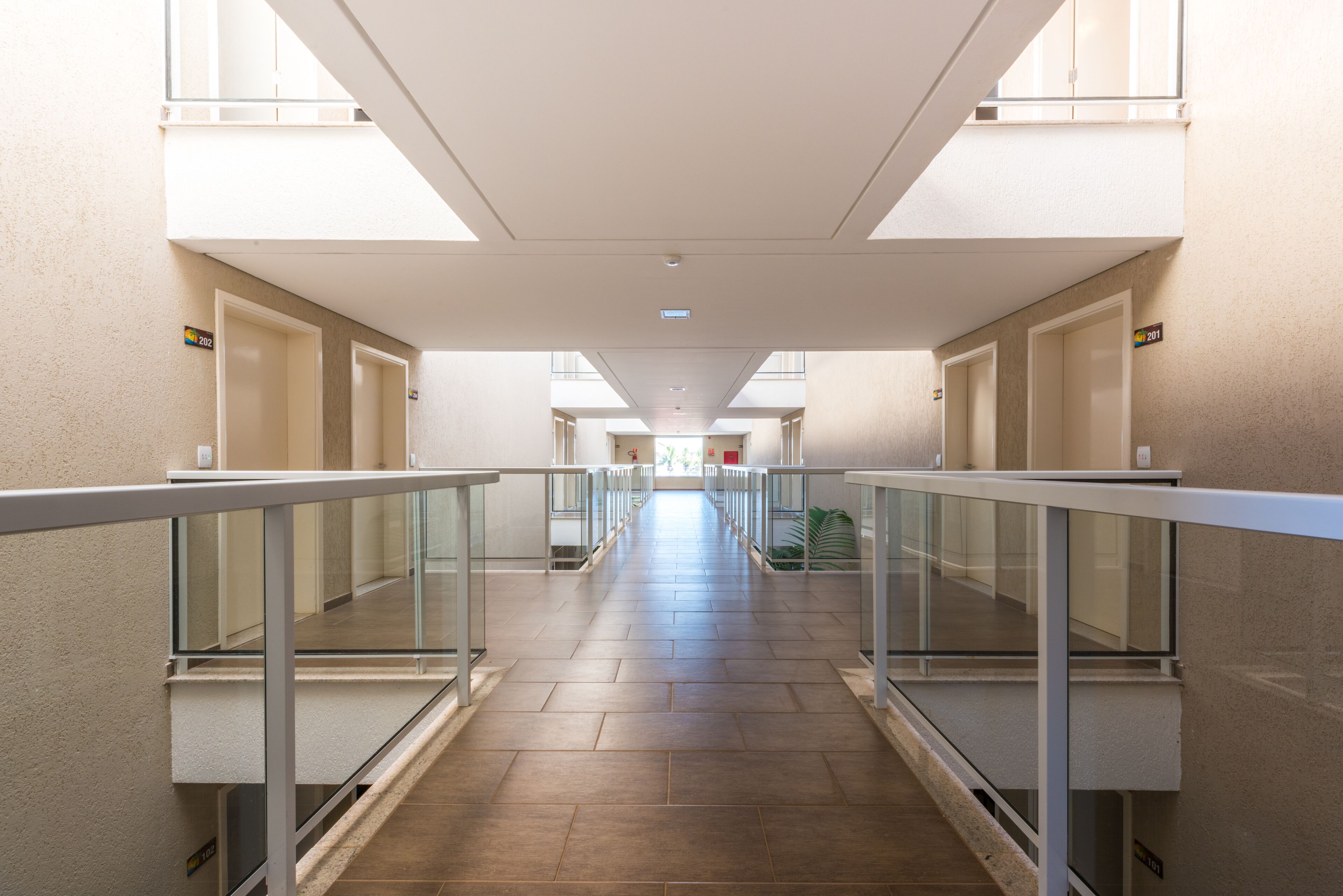 A long, narrow corridor with glass railings and tiled floors, leading to multiple doors on either side.