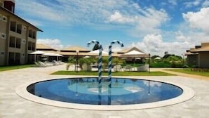 A swimming pool with two striped poles in the center, surrounded by a building with multiple balconies and outdoor seating areas. - Resort da Ilha (Sales)