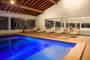 An indoor swimming pool with lounge chairs and tables, large windows, and a wooden ceiling. - Resort da Ilha (Sales)