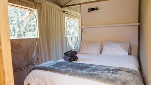 Een enkel bed met een witte matras en een grijze deken, een houten hoofdbord en een raam met gordijn.