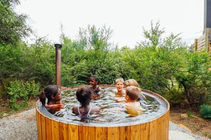 Un grupo de niños jugando en un jacuzzi de madera rodeado de follaje.