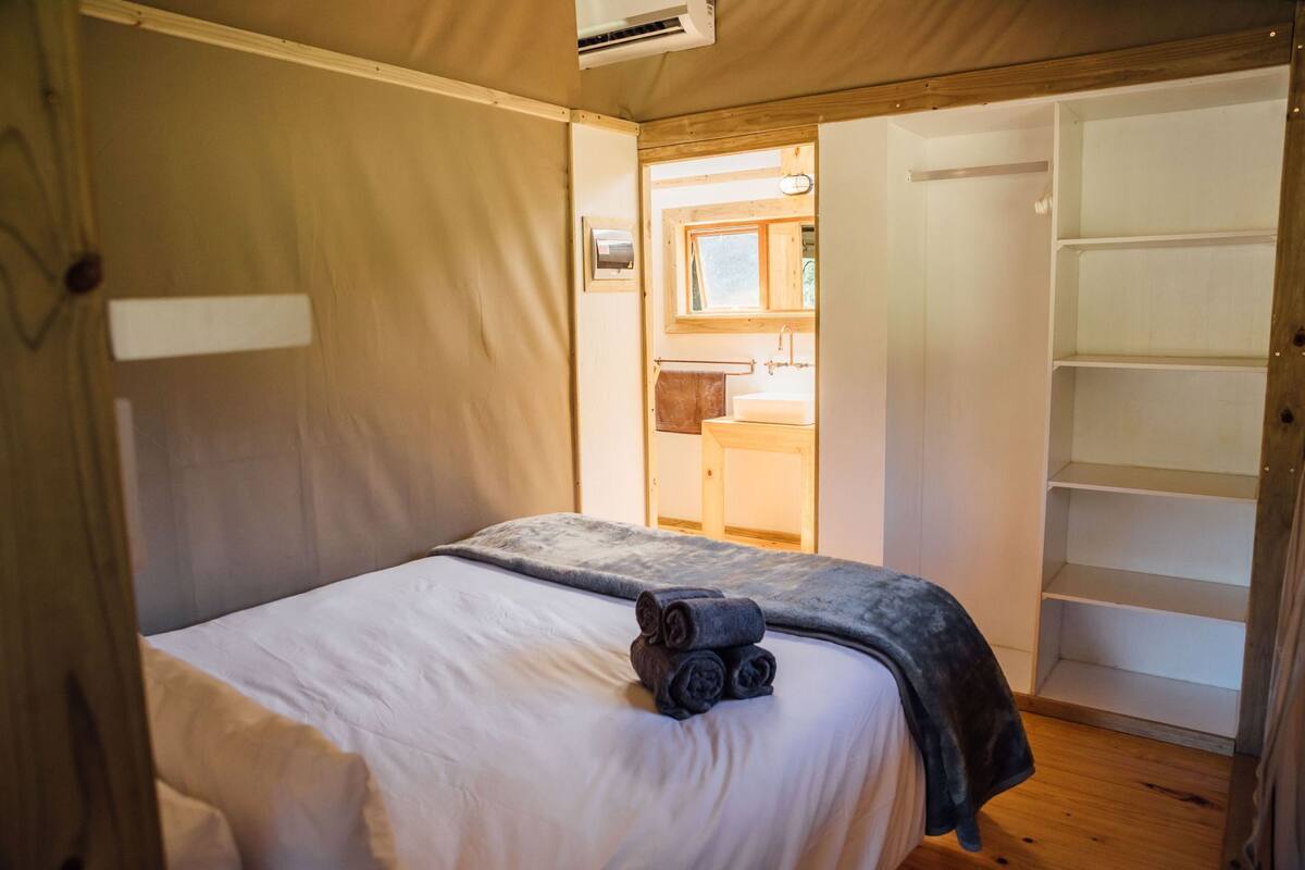 Een slaapkamer met een bed, een houten garderobe en een badkamer door een open deur zichtbaar.