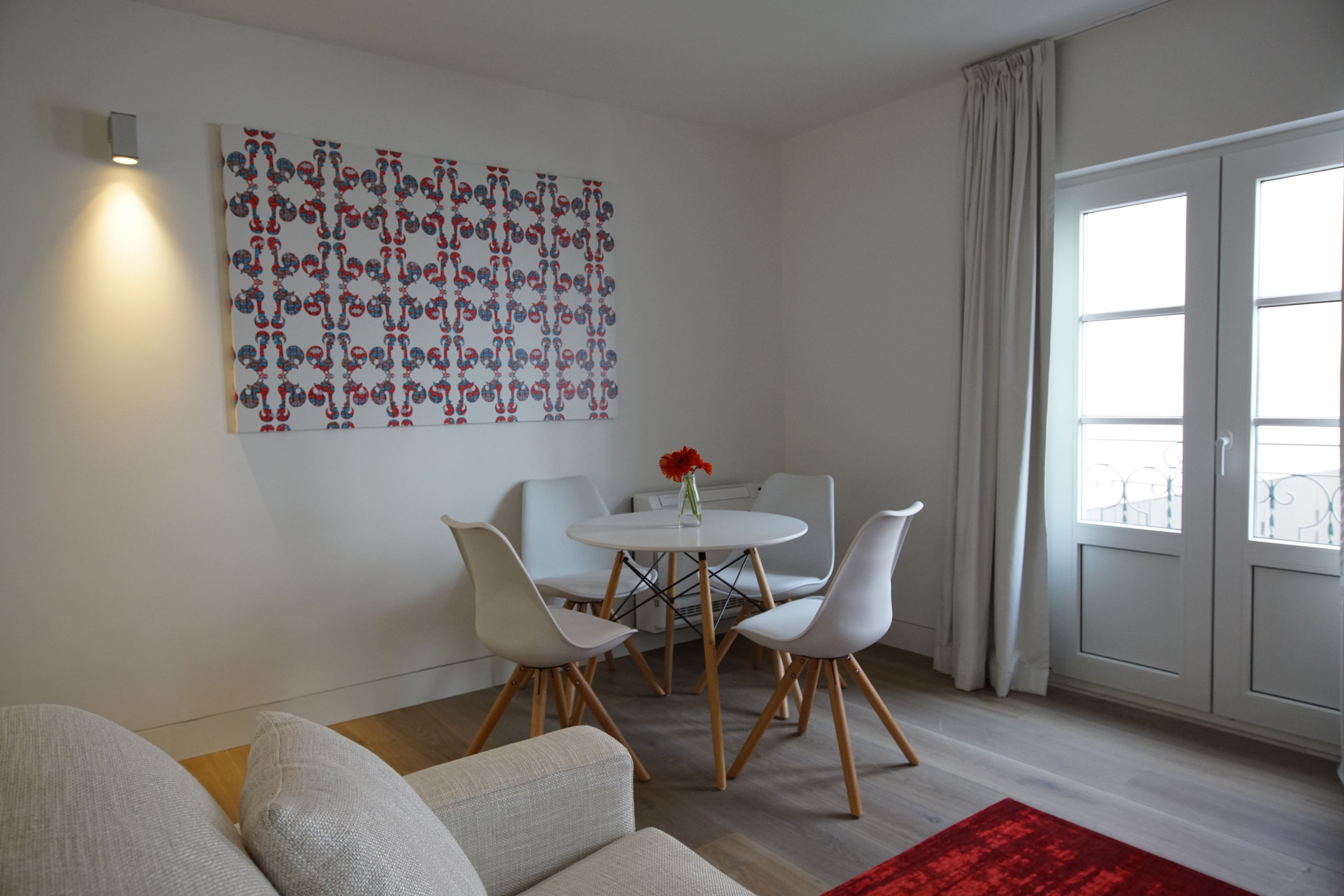 Una sala de estar moderna con comedor, que incluye un sofá blanco, un tapete rojo y una mesa con sillas.
