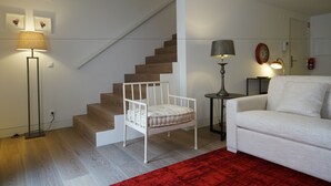 A living room with a staircase, a white sofa, a red rug, and two floor lamps. - Alma Moura Residences (Lisbon)