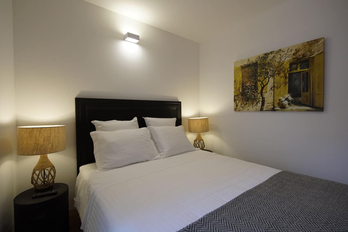 Un lit bien fait, avec du linge de lit blanc, deux lampes de chevet et un tableau accroché au mur.