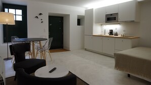 A compact living space with a kitchenette, a dining area with chairs, a bed, and a lamp. - Alma Moura Residences (Lisbon)