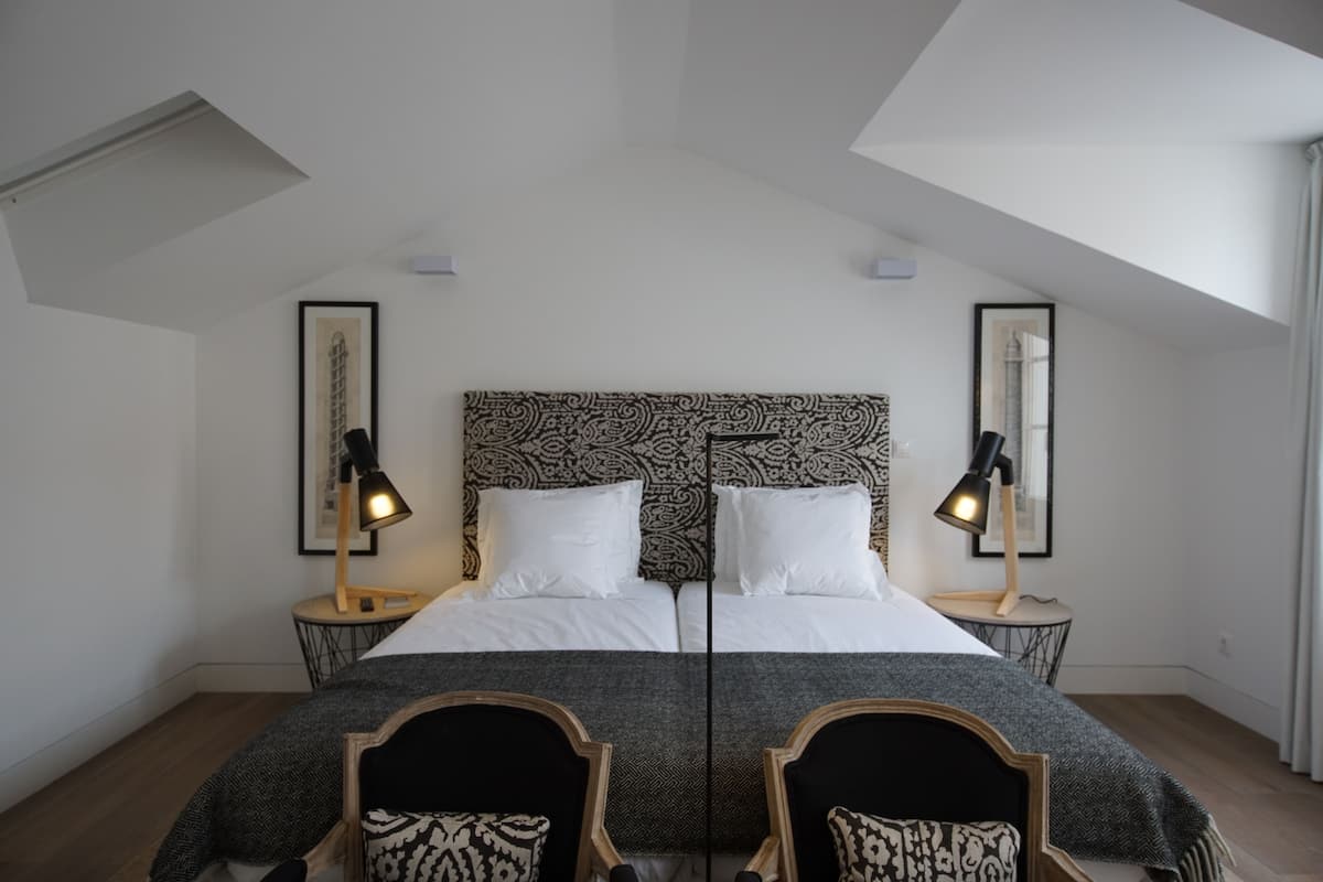 Une chambre à coucher avec un grand lit, deux tables de chevet avec des lampes, une tête de lit à motifs et un puits de lumière.