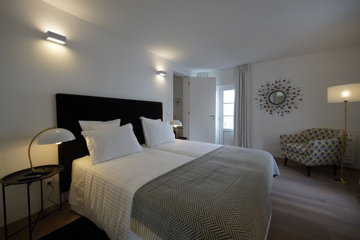 Une chambre d’hôtel avec un grand lit, une table de chevet avec une lampe, un fauteuil à motifs et un miroir décoratif au mur.