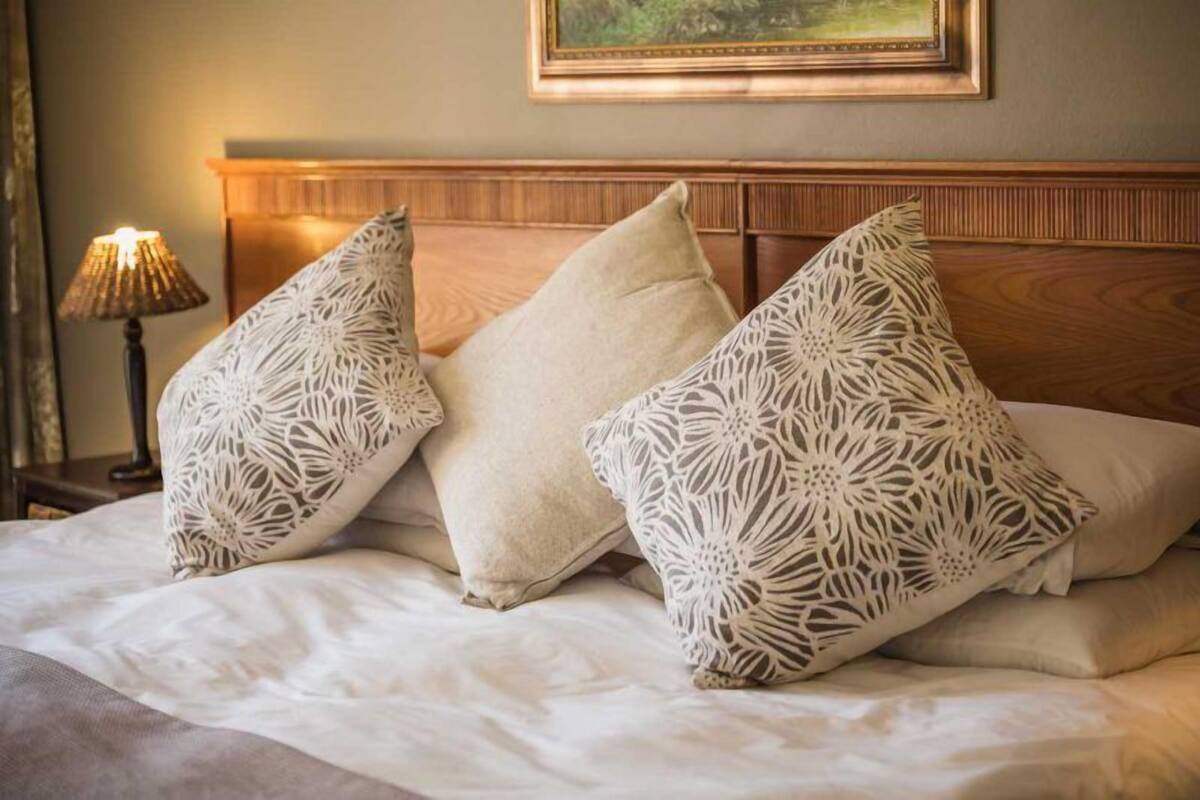 A neatly made bed with three patterned pillows and a wooden headboard.