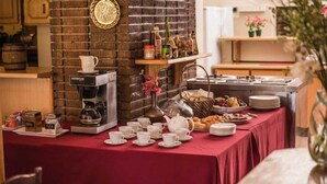 A breakfast buffet with coffee and tea stations, a brick wall, and a variety of food items. - Acacia Guesthouse (Klerksdorp)