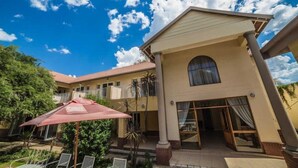 A hotel with a two-story structure, a covered outdoor seating area, and a clear blue sky. - Acacia Guesthouse (Klerksdorp)