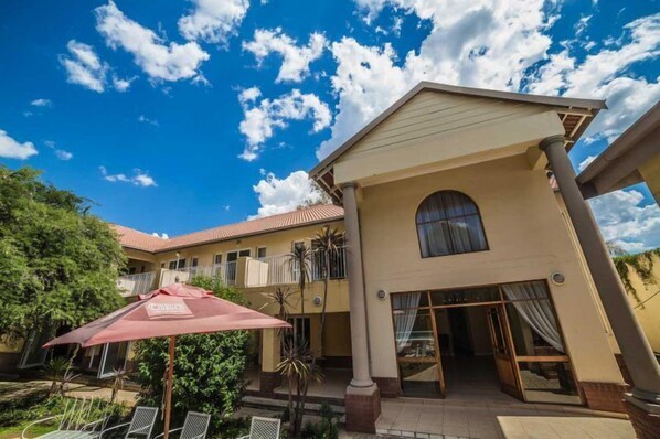 A hotel with a two-story structure, a covered outdoor seating area, and a clear blue sky. - Acacia Guesthouse (Klerksdorp)