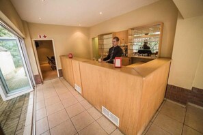 A reception area with a wooden counter, a person behind it, and a glass display case with items. - Acacia Guesthouse (Klerksdorp)