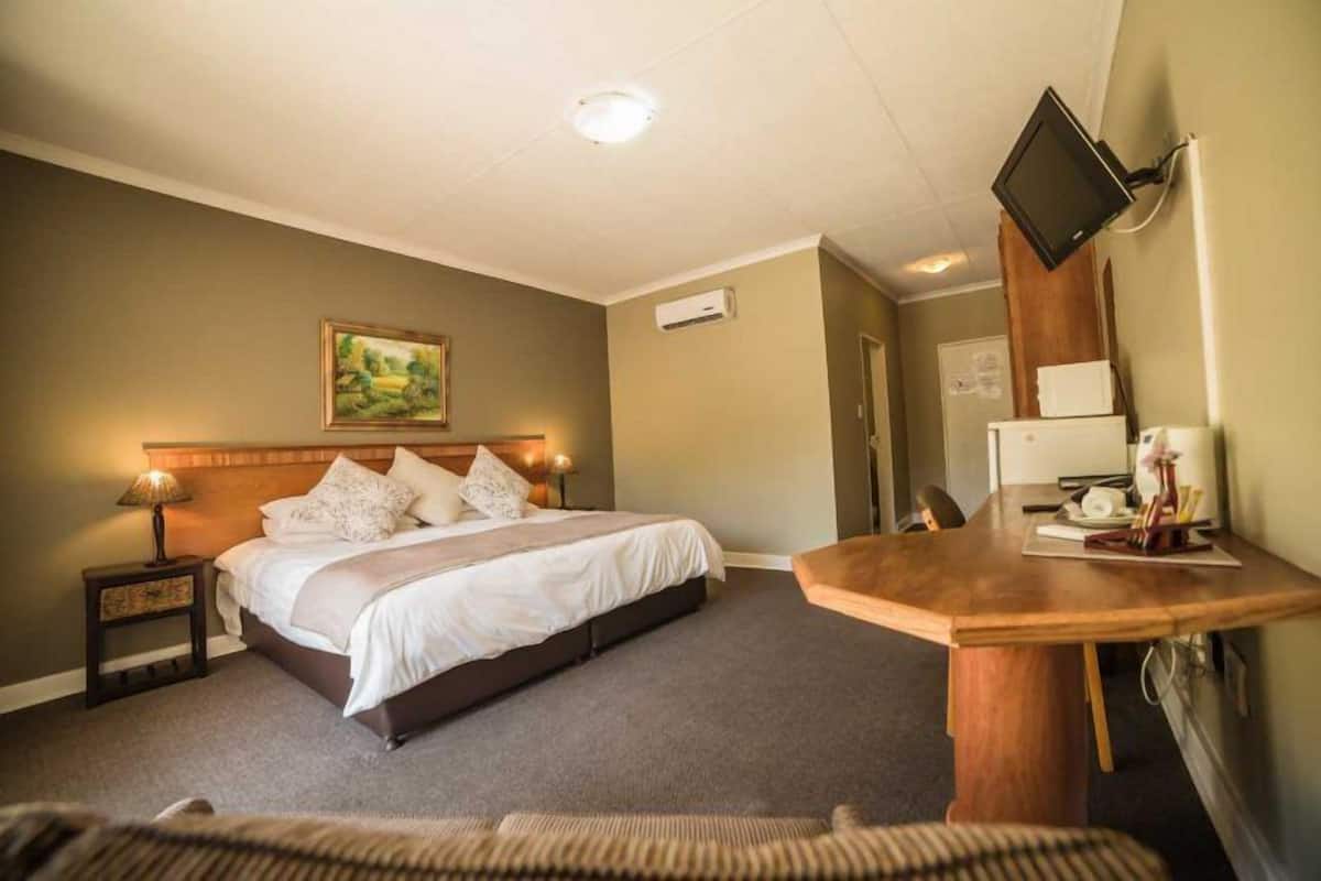 A hotel room with a bed, bedside table, lamp, and a TV mounted on the wall.