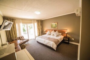 A hotel room with a bed, a desk, a chair, a TV, and a window with curtains. - Acacia Guesthouse (Klerksdorp)