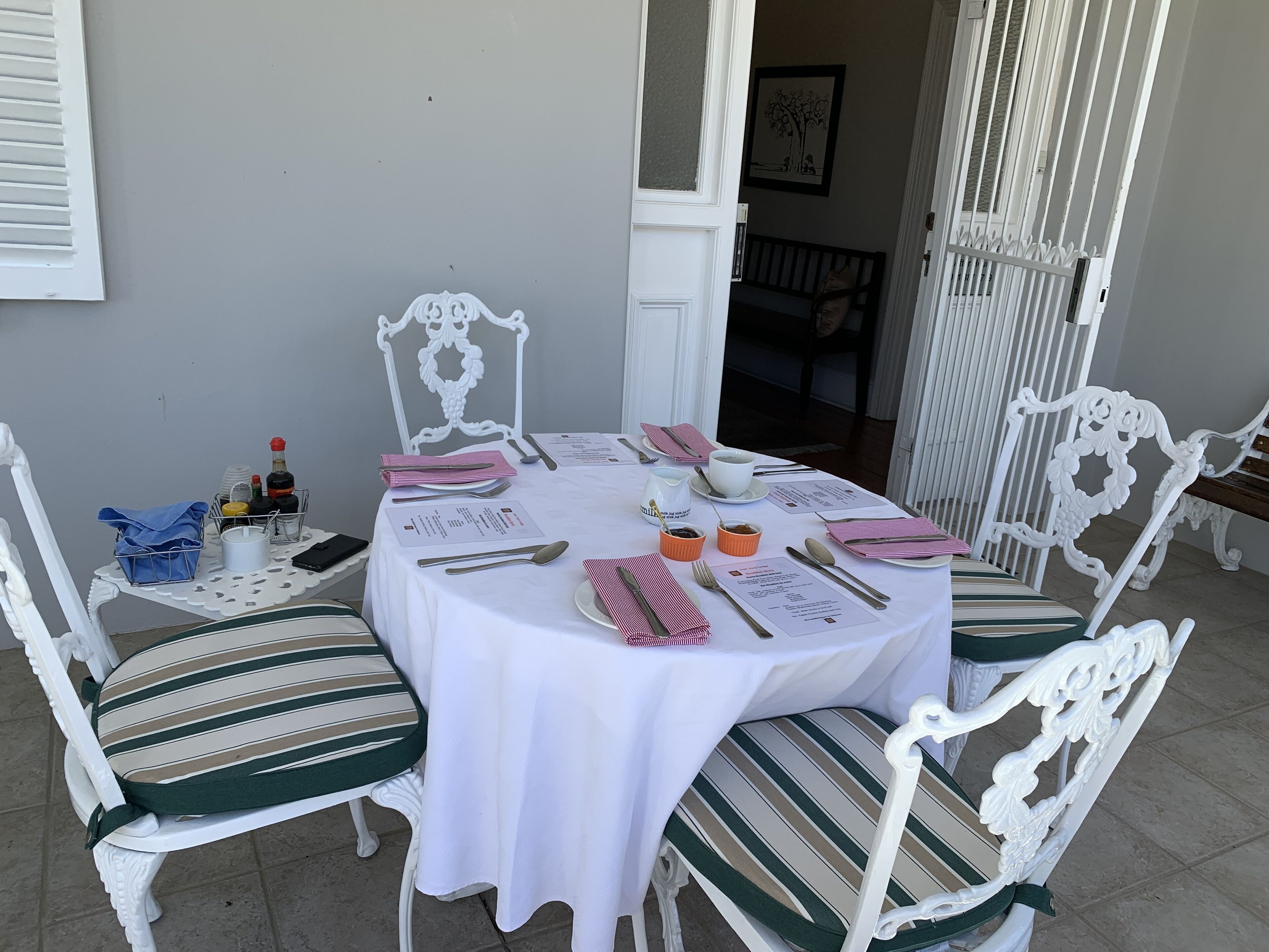 A round dining table set for four with white tablecloth, striped chairs, and a white decorative chair.