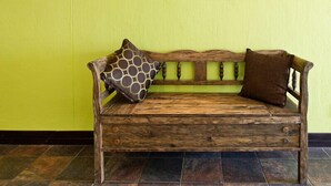 A wooden bench with a backrest and two cushions against a yellow wall. - Galton House (Windhoek)