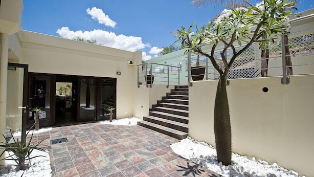 A modern building with a tiled patio, a staircase, and a fenced area with plants. - Galton House (Windhoek)