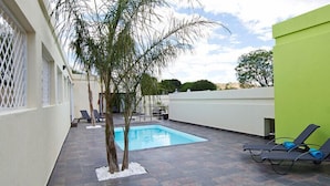 A pool area with a small pool, lounge chairs, and a tree. - Galton House (Windhoek)