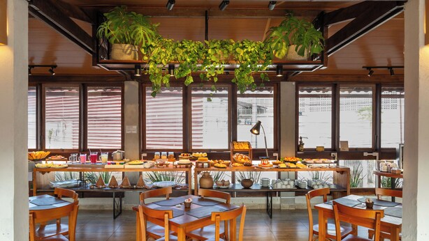 Un espace repas avec des tables et des chaises en bois, un buffet proposant divers plats et des plantes en pot suspendues au plafond.