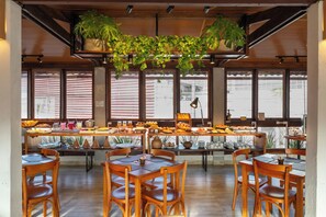 A dining area with wooden tables and chairs, a buffet with various food items, and potted plants hanging from the ceiling. - Pousada Jangadeiro (Porto Seguro)